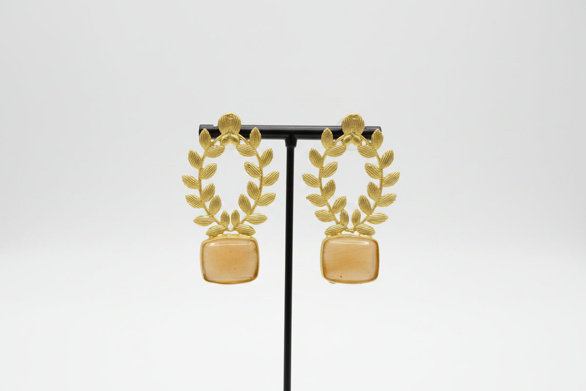 Statement earrings featuring an peach sugar stone with detailed floral carvings and golden accents on a stand.