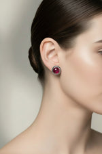A pair of silver-toned stud earrings with oval deep red gemstones and twisted silver borders, displayed on a white marble block.