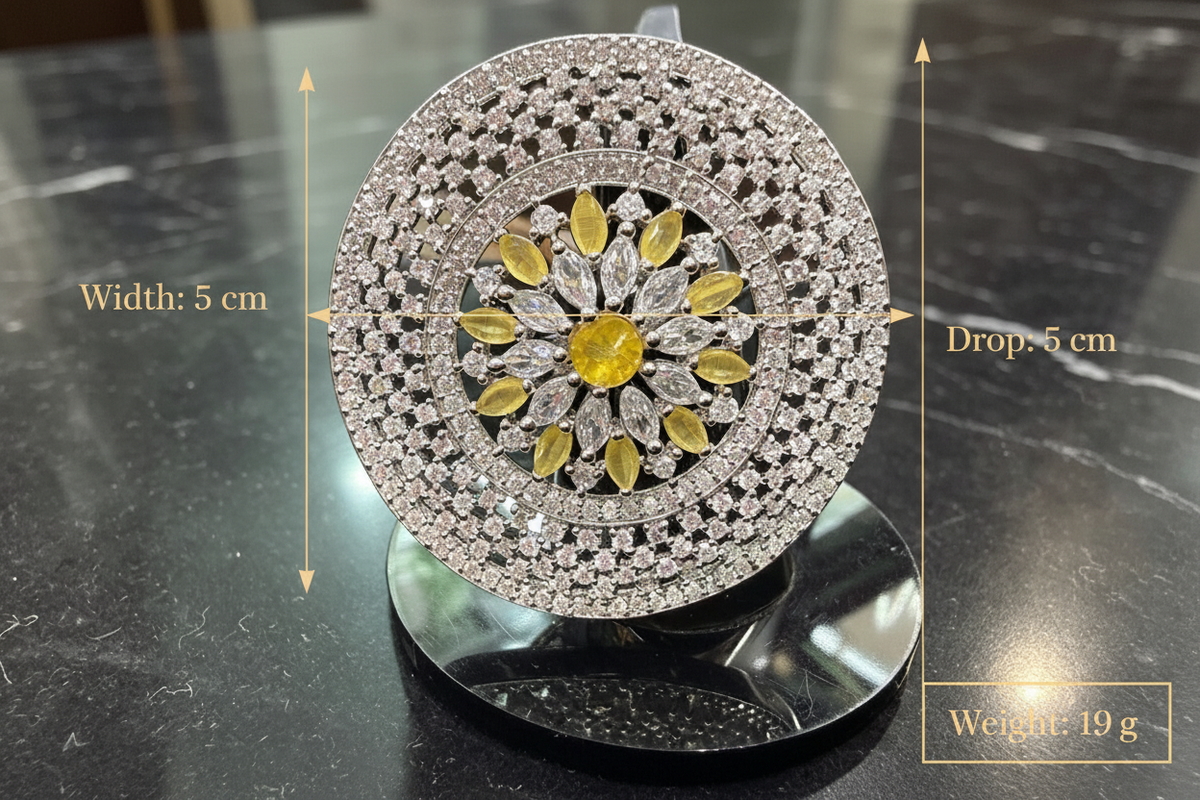 A round pavé diamond jewelry stand or display piece shown on a dark marble surface, with measurement arrows and text indicating a diameter of 5 cm, drop of 5 cm, and weight of 19 g. The center features a yellow floral motif surrounded by clear stones.