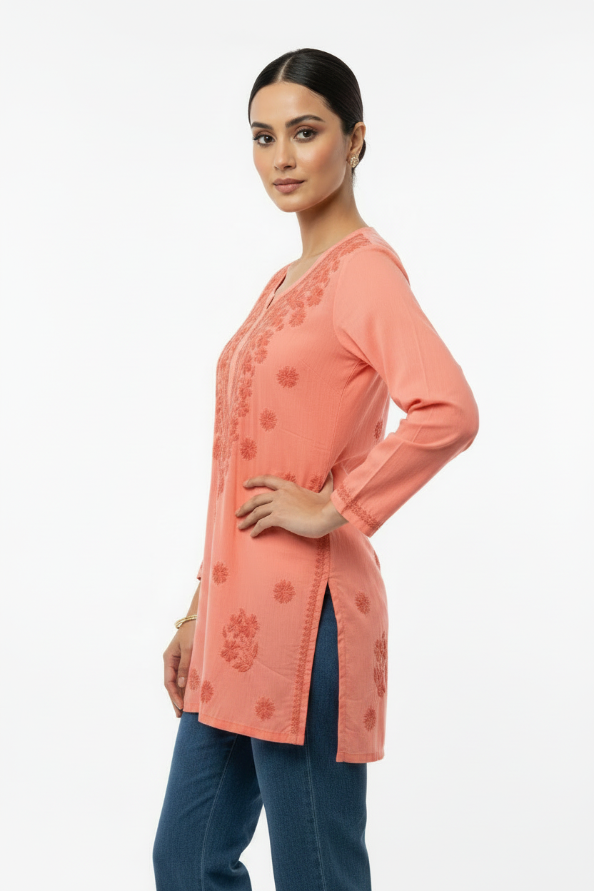 A side profile view of a model wearing a peach short kurti featuring floral embroidery details and side slits, paired with white trousers.