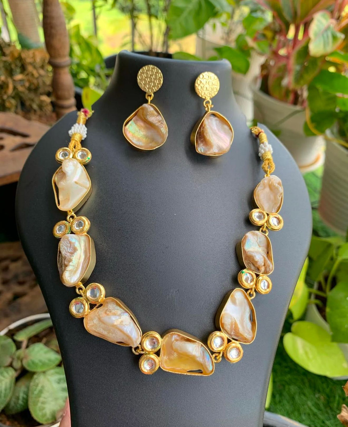 A Baroque pearl choker necklace with square-shaped mother of pearls and kundan accents, paired with matching earrings, against a black background.