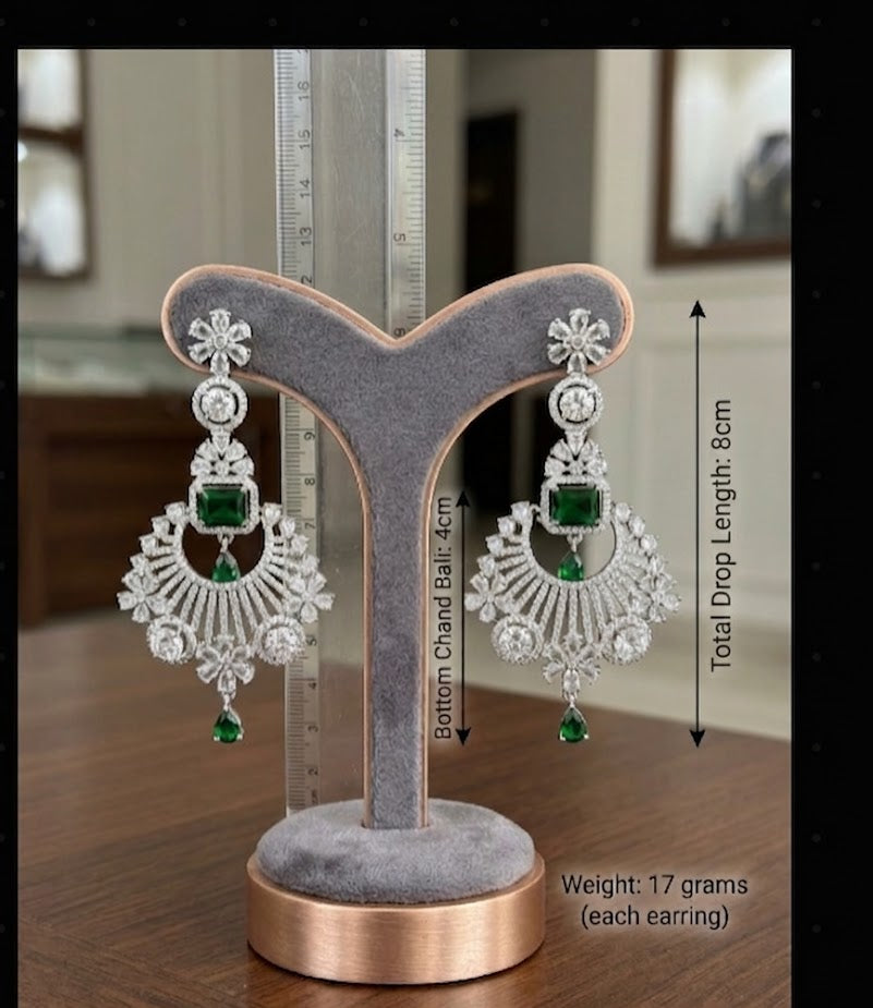 Elegant silver-toned chandelier earrings featuring sparkling cubic zirconia stones and vibrant green emerald-cut center stones, with a total drop length of 8cm, displayed on a jewelry stand.