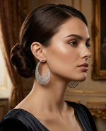 Woman in a black dress wearing sparkling 'High-Jewellery Collection' diamond lattice earrings, shown against a classic palace backdrop.
