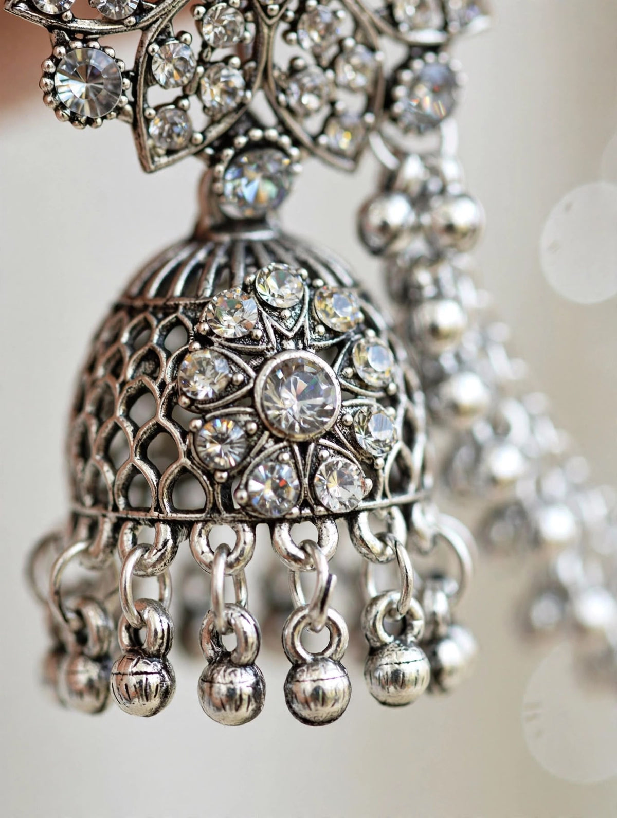 Silver-toned ornate jhumka earrings with clear rhinestones and dangling bead chains, shown in a close-up studio shot.