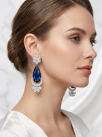 Silver-toned chandelier earrings featuring a massive royal blue teardrop stone accented by crystal floral motifs and a glittering crescent base.