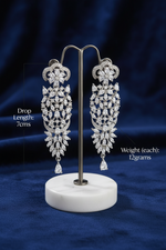Elegant long silver statement earrings intricately set with brilliant marquise and teardrop cubic zirconia crystals, showcased on a luxury retail display stand in