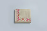 The beige shawl with floral patterns draped over a mannequin next to a black handbag on a small table against a marble wall.