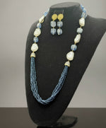 Theblack mannequin showcasing a Bollywood style Navy blue colour Mona Lisa stone and Navyblue colour nano crystal beaded Mala set, with white colours of baroque pearls and gold-tone accents. Party wear jewellery set. 