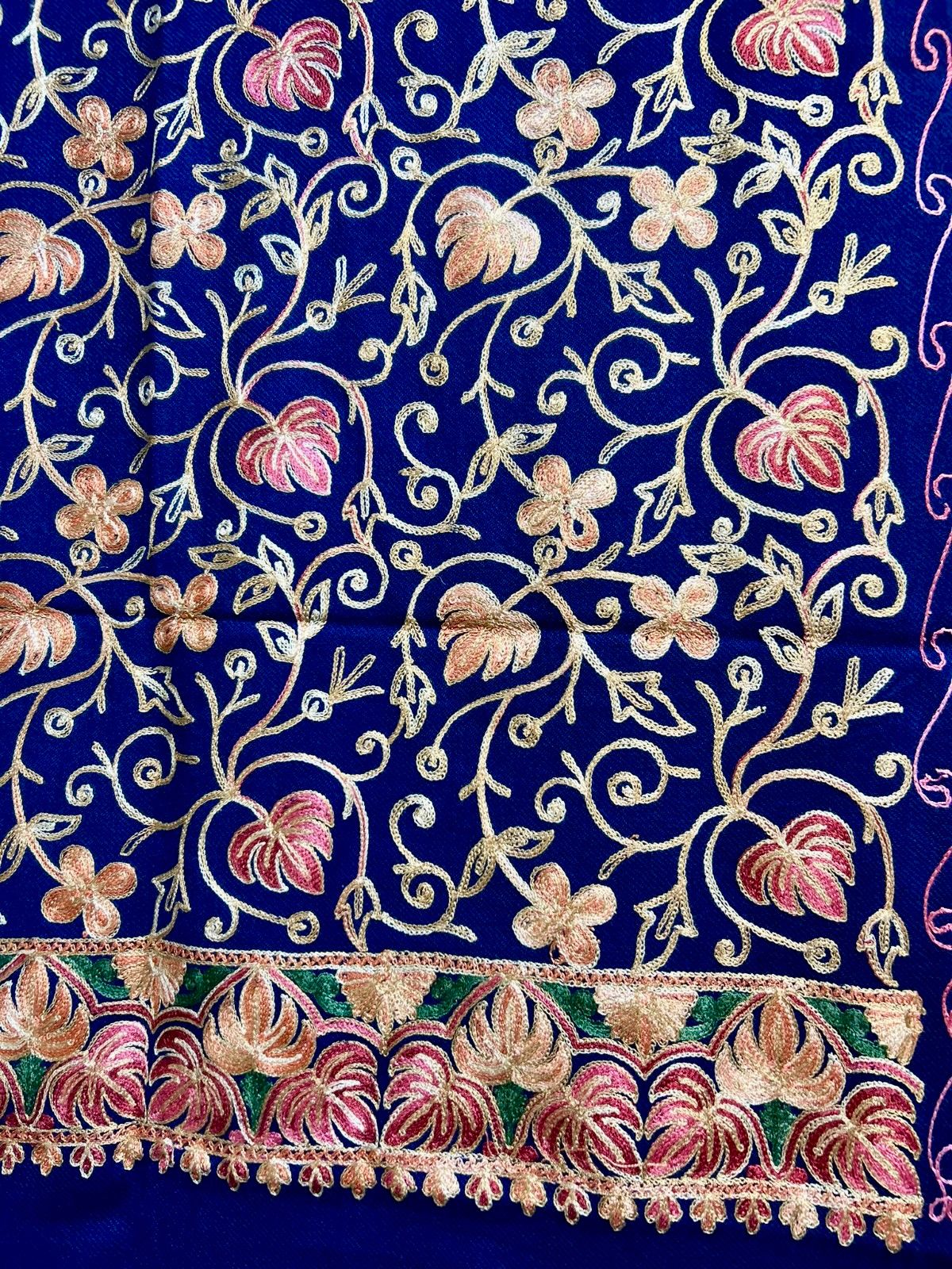 The blue Kashmiri embroidered pashmina scarf with maple leaf motifs and tassels on the ends, displayed on a wooden surface.