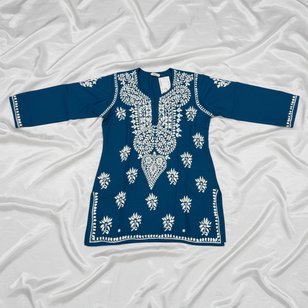The deep dark teal colour code is #215D6E tunic dress with intricate white floral and geometric block-print embroidery, laid flat on a grey wood-look floor.