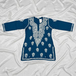 The deep dark teal colour code is #215D6E tunic dress with intricate white floral and geometric block-print embroidery, laid flat on a grey wood-look floor.