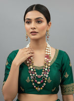 The gold-plated Kundan-studded and pearl-beaded handcrafted jewellery set, consisting of a necklace and earrings, displayed against a black background.