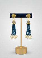 The gold-plated Kundan-studded and pearl-navy blue beaded handcrafted earrings, displayed against a black background. 