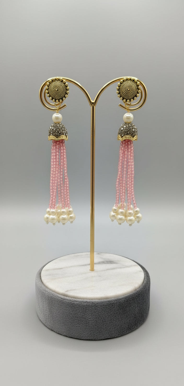 The gold-plated Kundan-studded and pearl-pink colour beaded handcrafted earrings, displayed against a black background. 