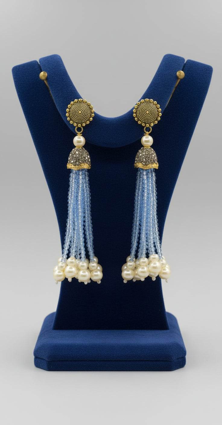 The gold-plated Kundan-studded and pearl-sky blue beaded handcrafted earrings, displayed against a black background. 
