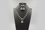 The mannequin showcasing a necklace set with bottle green and white stones, accompanied by earrings and a maang tikka. Party wear set. 
