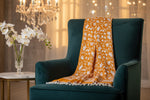 The orange Kashmiri pashmina scarf with white floral embroidery and tassels hanging at the ends, displayed on a golden background.