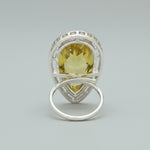 The rear view of a silver-toned ring with a teardrop-shaped yellow gemstone, displayed on a dark textured surface.