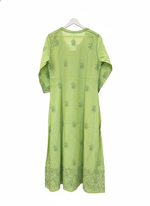 The rear view ofapple green dress with floral patterns on a grey surface with small decorative items.