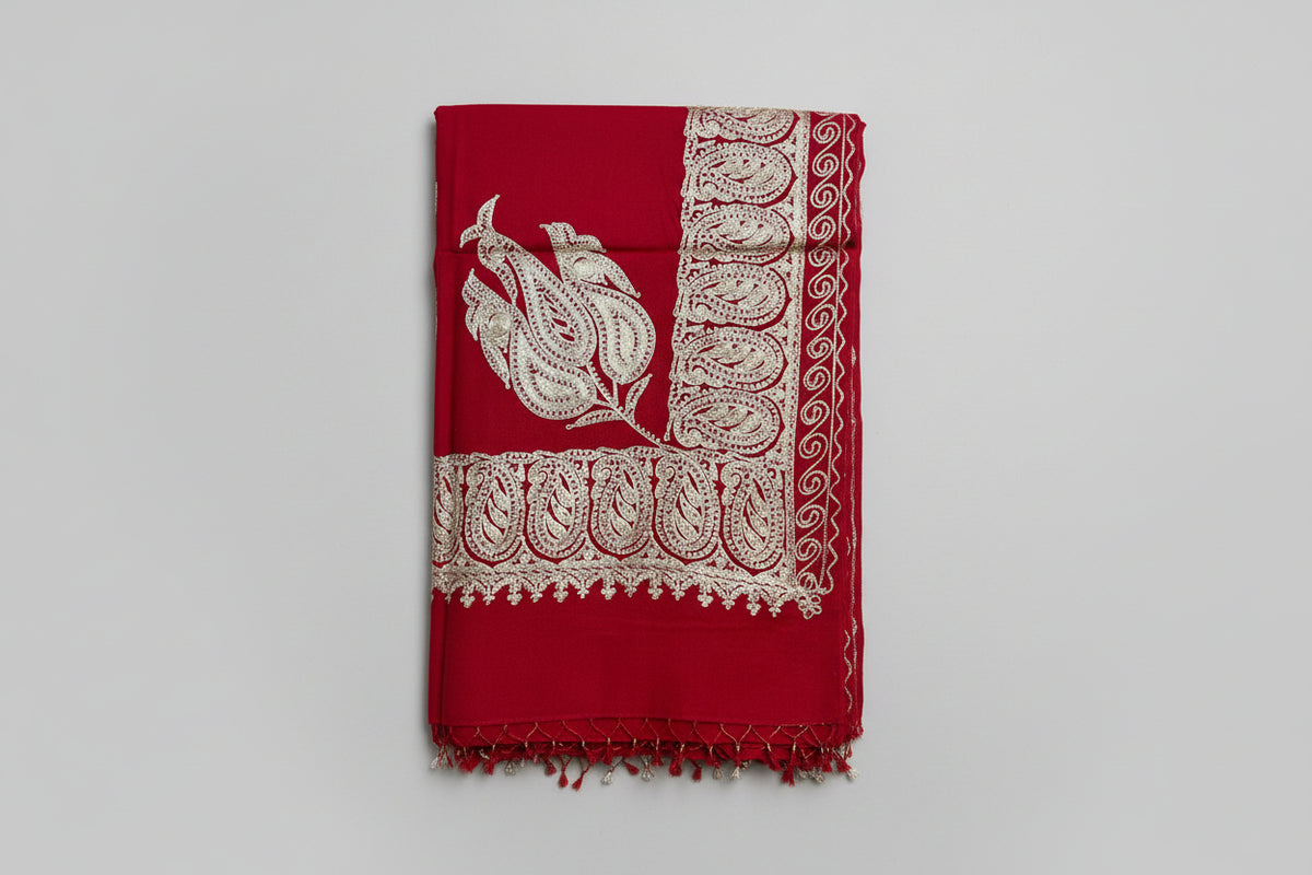 The red colour Kashmiri embroidered pashmina shawl with tassels on the ends, displayed on a wooden surface.