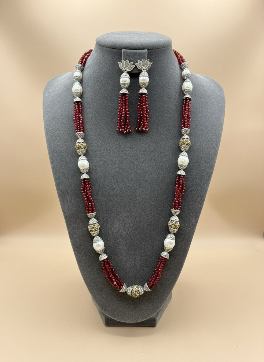 The set of jewellery featuring a long necklace with Red-coloured glass beads and metallic accents, paired with matching earrings, displayed on a mannequin bust. 