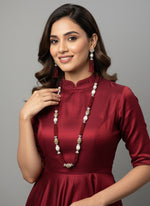 The set of jewellery featuring a long necklace with Red-coloured glass beads and metallic accents, paired with matching earrings, displayed on a mannequin bust. Party wear set. 