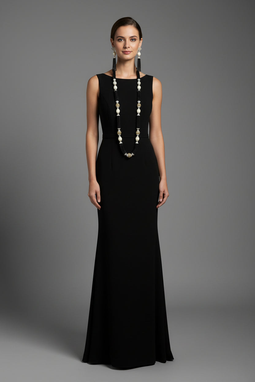 The set of jewellery featuring a long necklace with black-coloured glass beads and metallic accents, paired with matching earrings, displayed on a mannequin bust. Party wear set. 