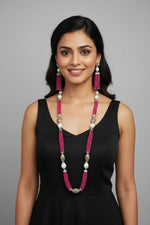 The set of jewellery featuring a long necklace with hot pink-coloured glass beads and metallic accents, paired with matching earrings, displayed on a mannequin bust. Party wear set. 