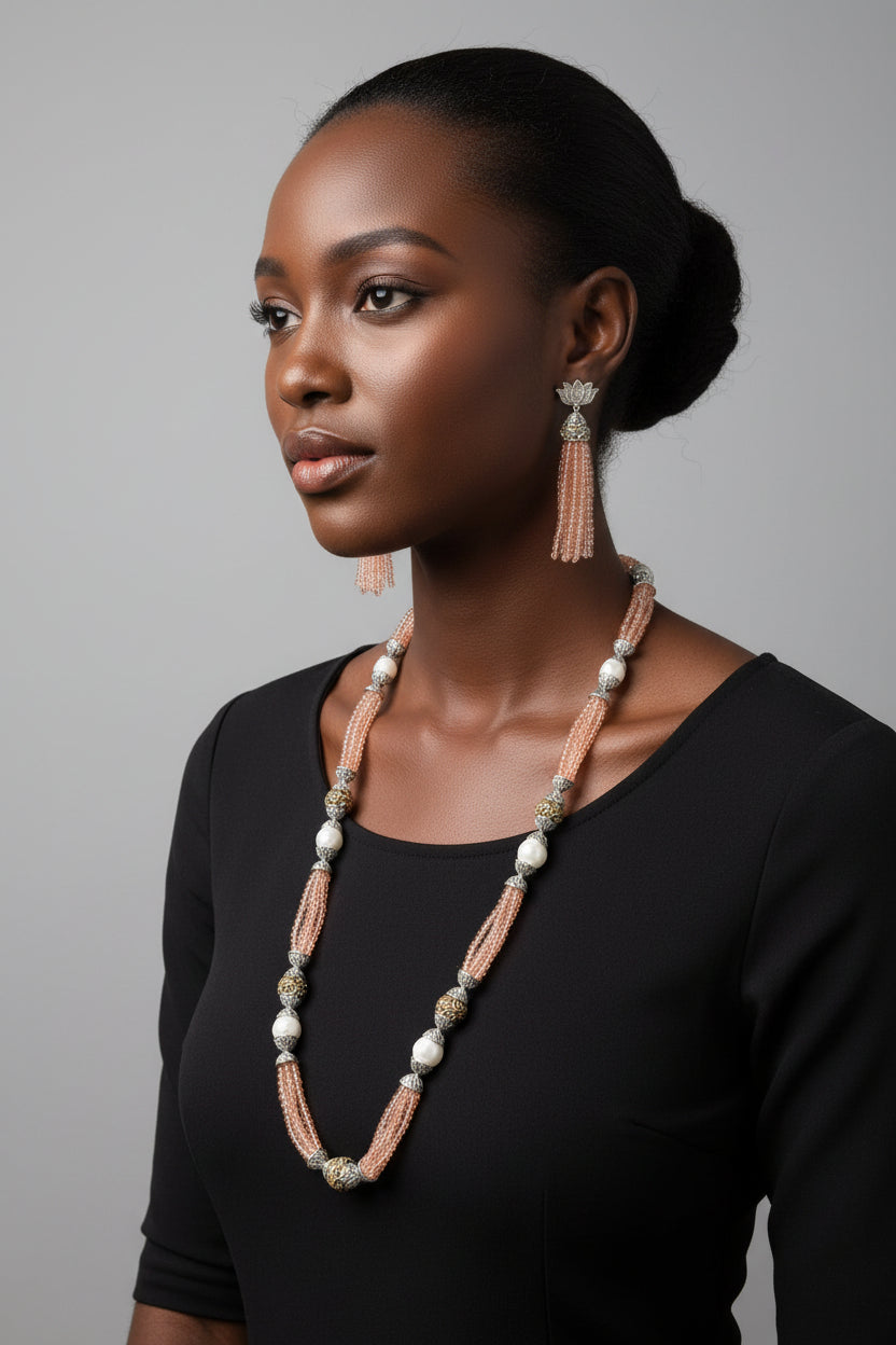 The set of jewellery featuring a long necklace with peach-coloured glass beads and metallic accents, paired with matching earrings, displayed on a mannequin bust. 
