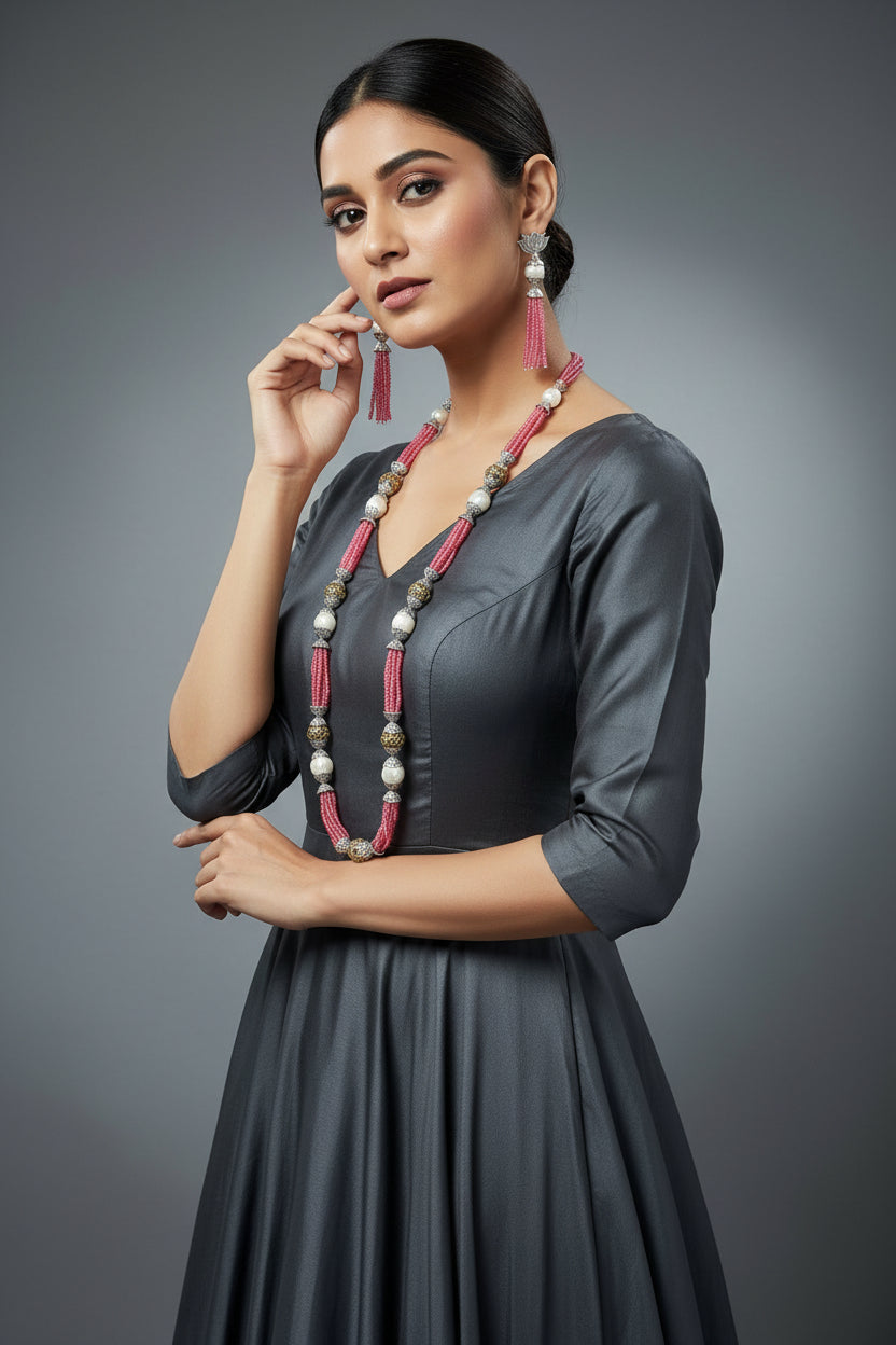 The set of jewellery featuring a long necklace with pink-coloured glass beads and metallic accents, paired with matching earrings, displayed on a mannequin bust. Party wear set. 