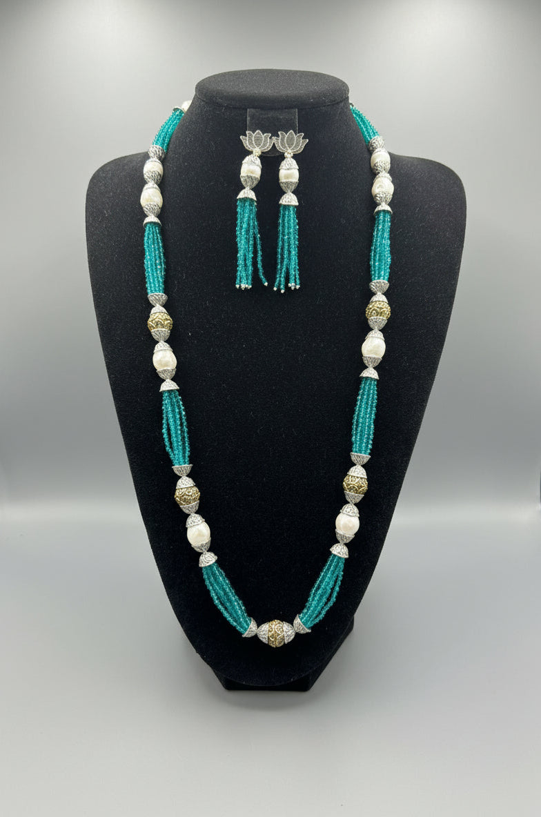 The set of jewellery featuring a long necklace with sky blue-coloured glass beads and metallic accents, paired with matching earrings, displayed on a mannequin bust. 