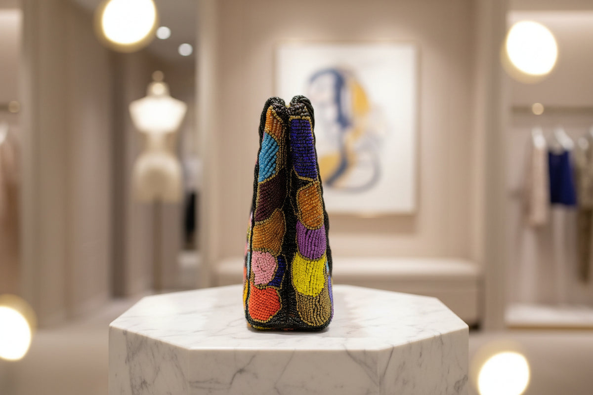 The side view of a multi-coloured circular handcrafted tote bag with glass beads, displayed on a wooden surface with foliage in the background