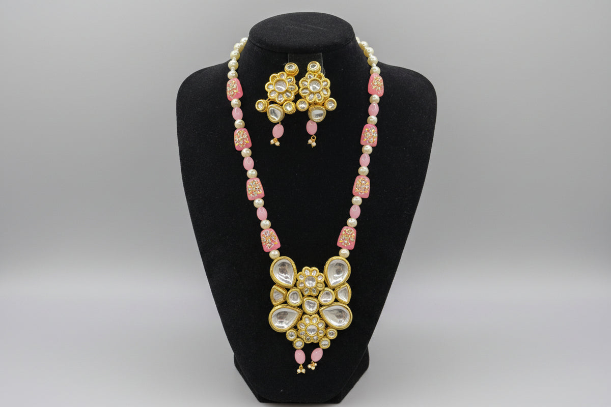 The traditional bridal necklace set displayed on a mannequin, featuring pink and gold colours with intricate detailing and pearl beads. Party wear jewellery set. 