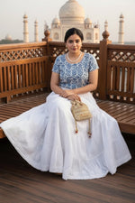 A woman wearing a long white tiered maxi skirt white rayon skirt with white Ghasspati hand embroidery on the bottom two layers and the hem is adorned with white crochet lace