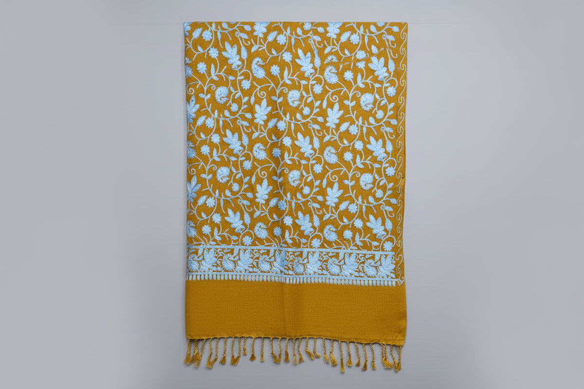 This orange Kashmiri embroideredpashmina scarf with white floral patterns and tassels on the ends, displayed against a golden background.