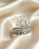 Fan Halo Tiered Ring with white crystal fan halo and silver & black multi-tiered band, luxury designer jewelry resting on cream satin fabric.