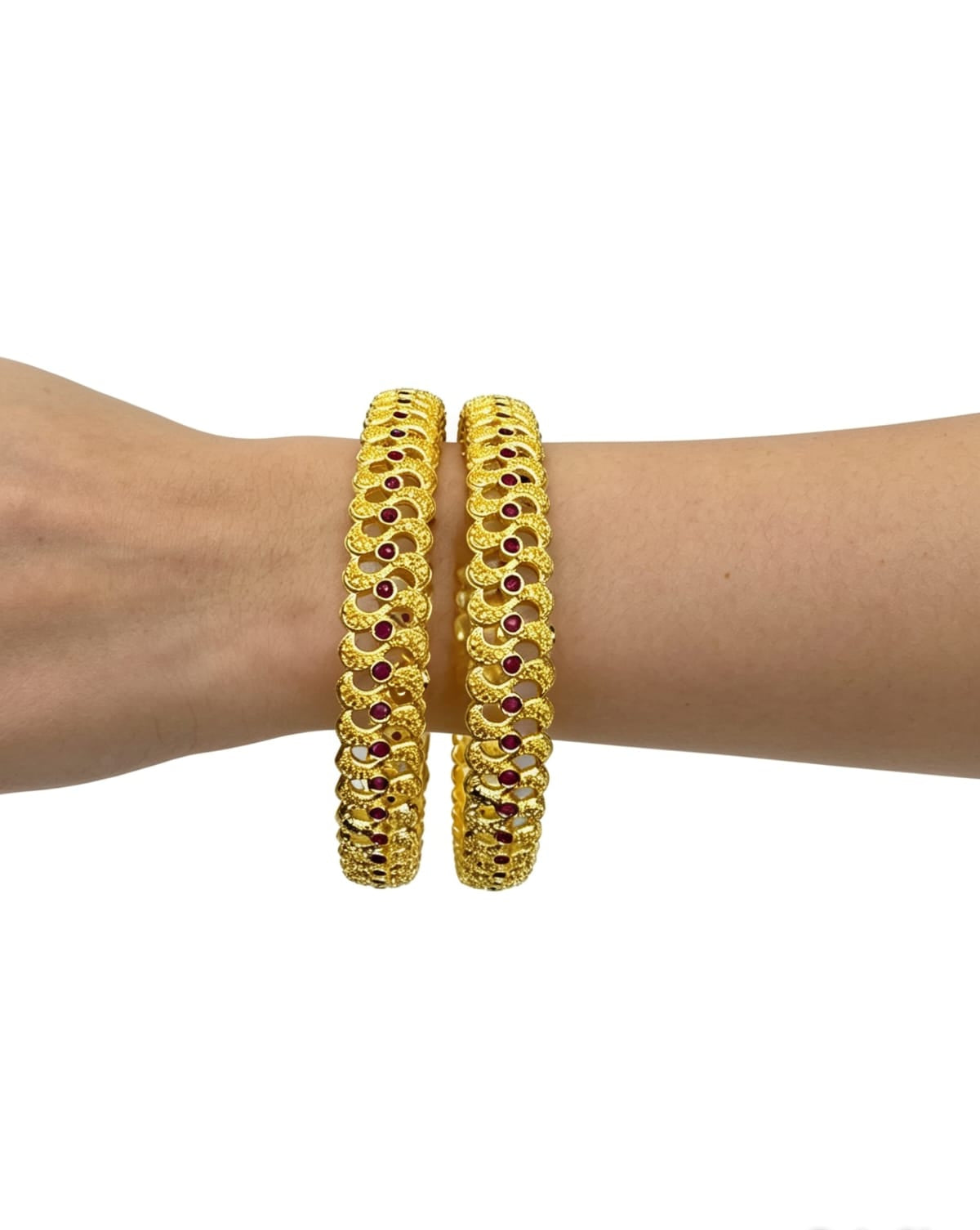 Close-up view of two ruby red stone-studded gold bangles worn on a wrist to showcase the textured floral lattice design.