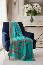 Turquoise Kashmiri Aari embroidered marina scarf with tassels hanging at the ends, displayed on a wooden hanger with greenery in the background.