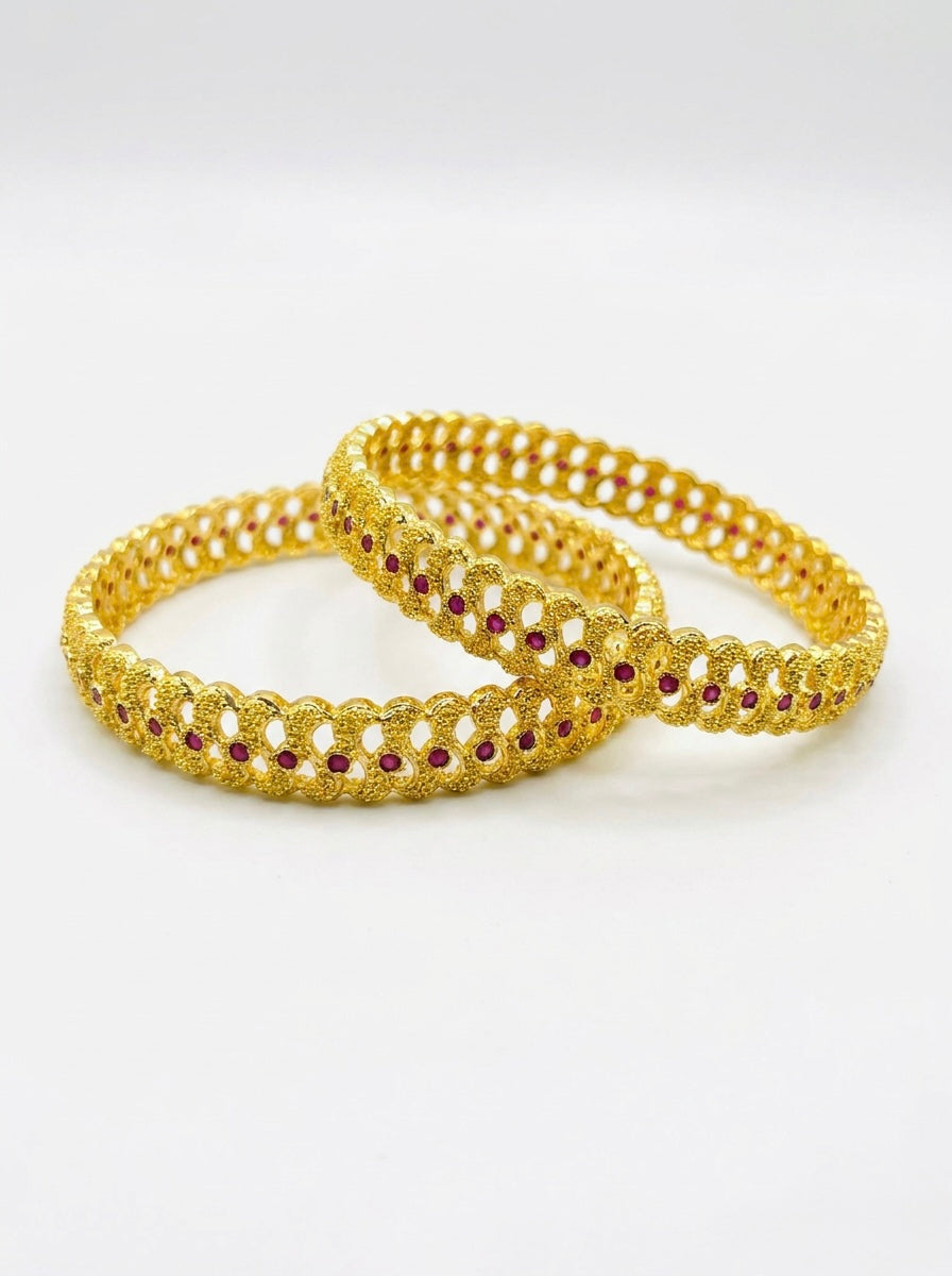 Two gold bangles with red stones on a white background