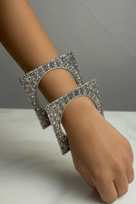 Two ornate silver-toned bangles with intricate filigree patterns and small clear stones, worn on a person's wrist against a light marble-like background.