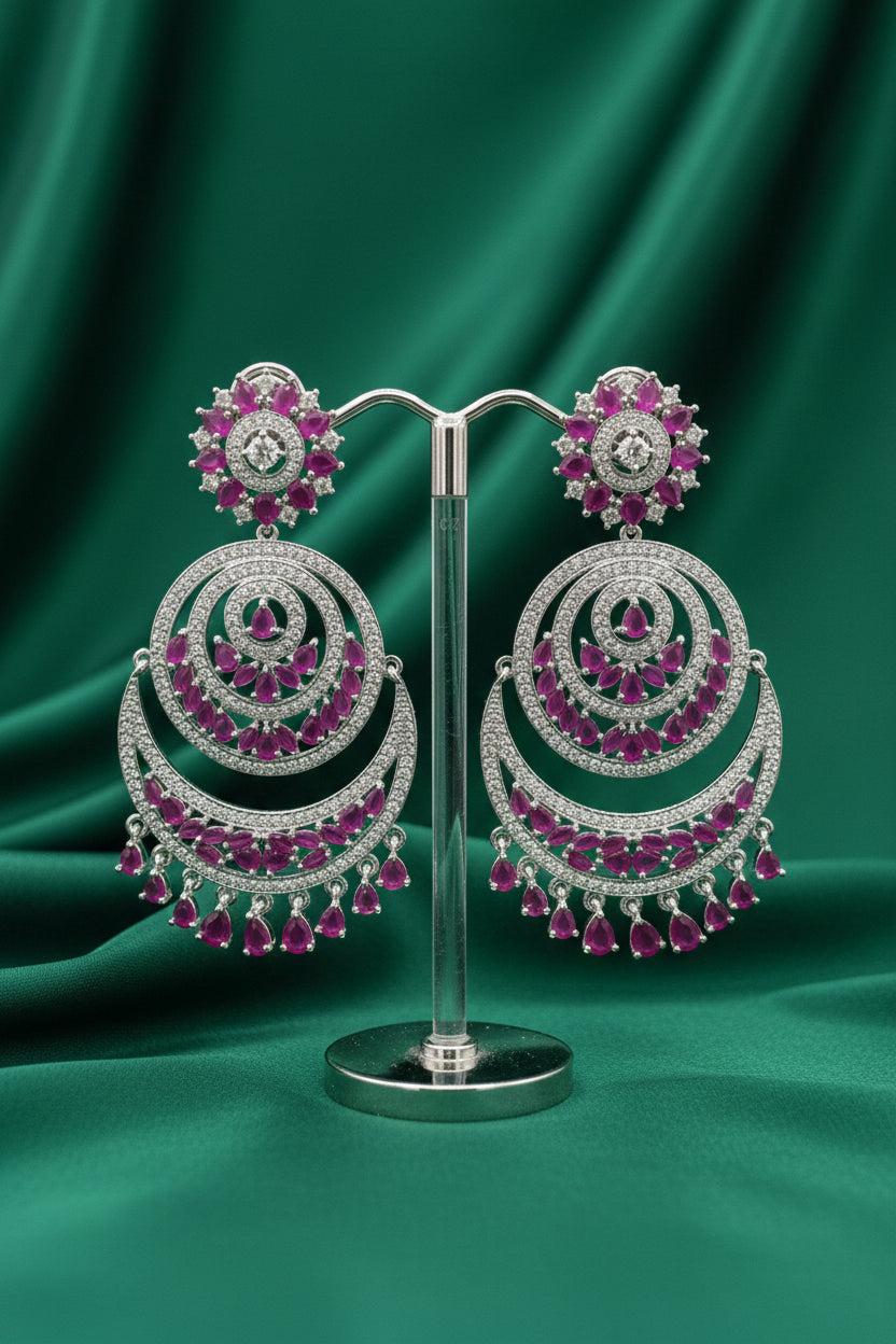 A pair of Royal Fuchsia Crescent Statement Dangle Earrings displayed on a stand, showcasing intricate silver-tone metalwork with vibrant fuchsia stone embellishments.