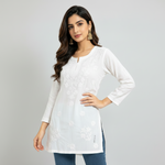 A woman modeling a white long-sleeve embroidered kurta with a split neckline and subtle floral embroidery, paired with matching white pants, against a plain white studio background.