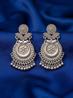 A pair of ornate silver-toned traditional earrings with intricate filigree, floral motifs, and dangling bead chains, displayed on a draped royal blue fabric background.