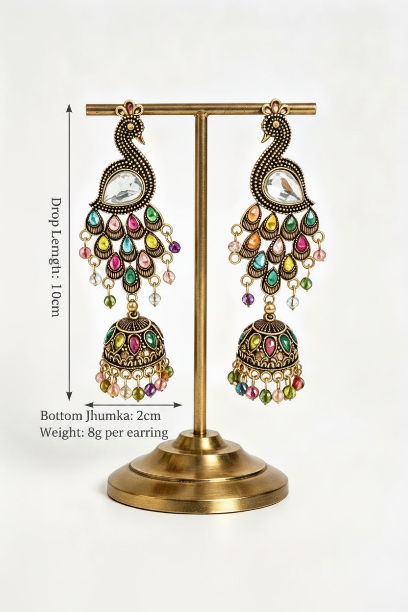 Product display view of Vintage Peacock Glow antique gold-plated multistone jhumka earrings hanging on a gold stand, showcasing drop length and weight specifications.
