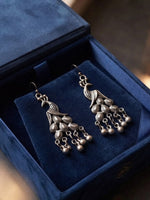 A pair of silver-toned traditional Indian dangle earrings displayed inside an open dark blue velvet jewelry box.