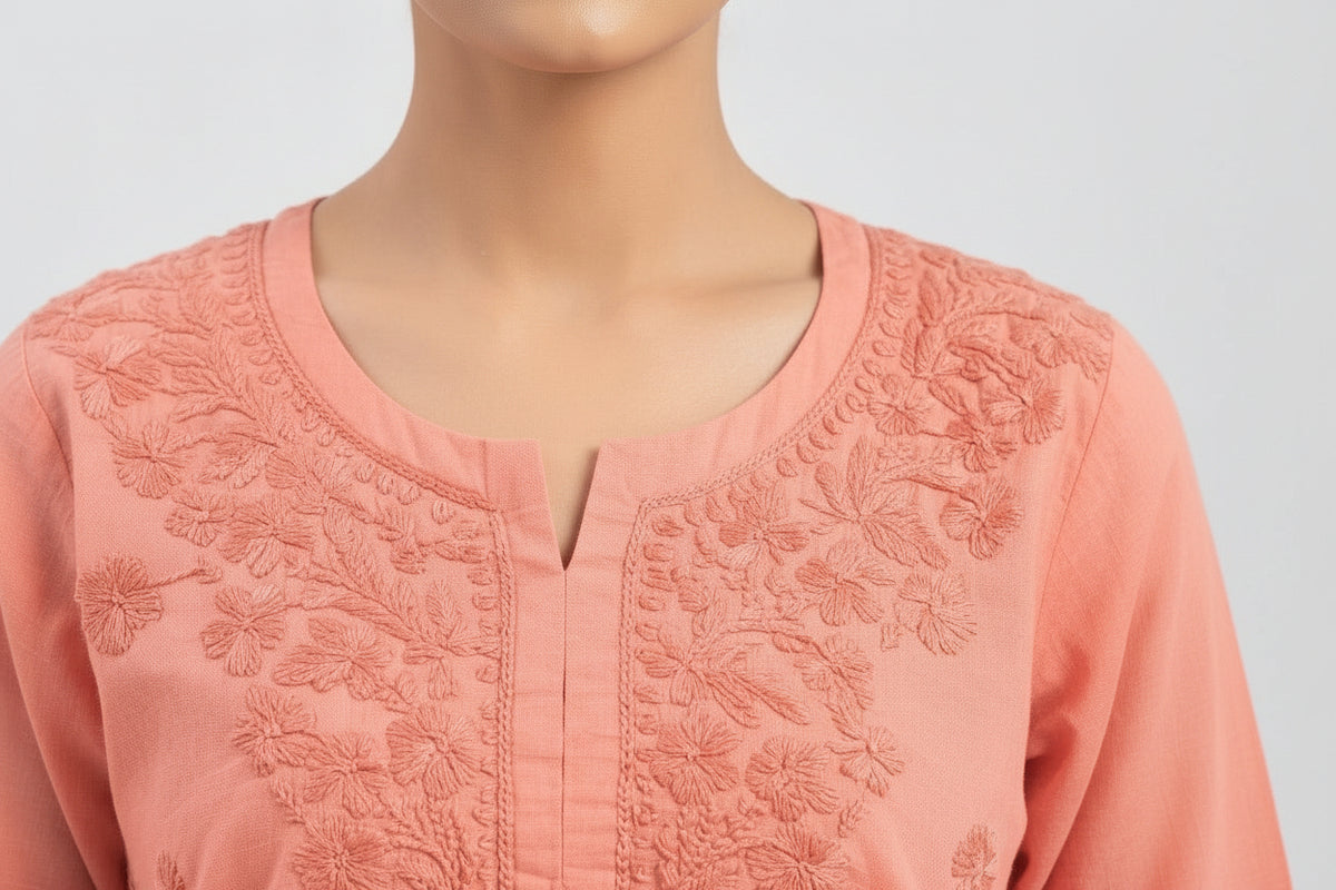 A close-up view of the neckline and yoke of a watermelon pink short kurti showcasing dense, intricate tonal embroidery around a split round neckline.