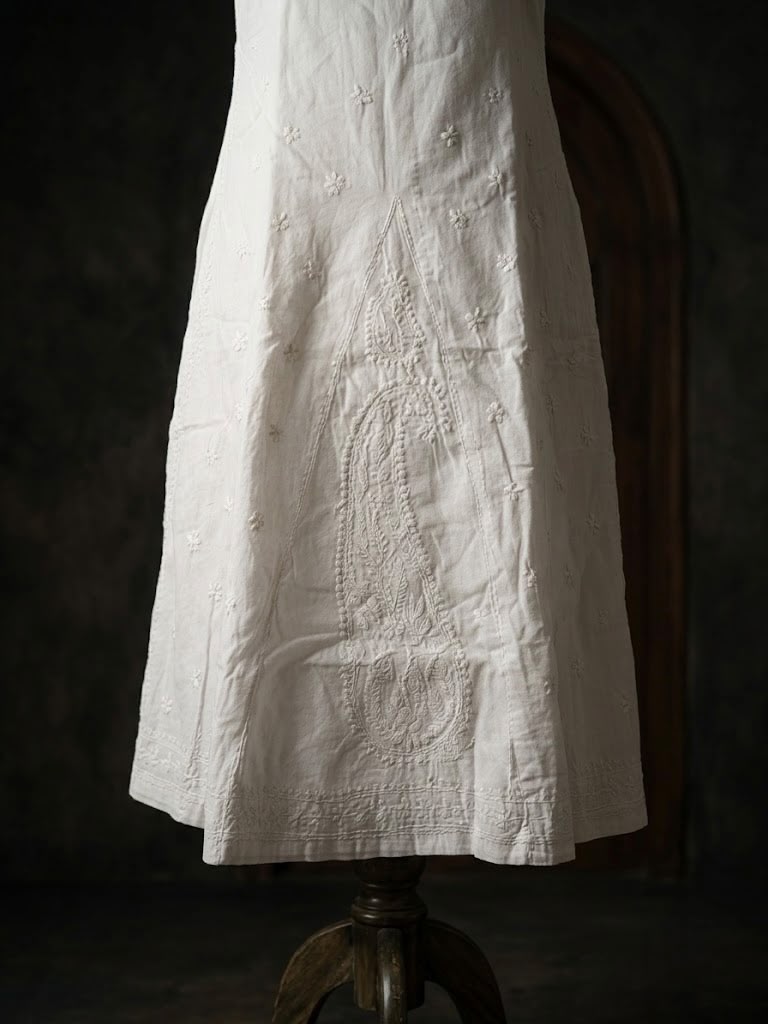 White cotton gharara featuring intricate traditional bakhiya embroidery, wide flared design, displayed on stand.