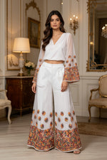 Model wearing a white georgette co-ord set featuring a v-neck top with wide sleeves and matching wide-leg plazo pants, both adorned with intricate multi-colour floral embroidery.