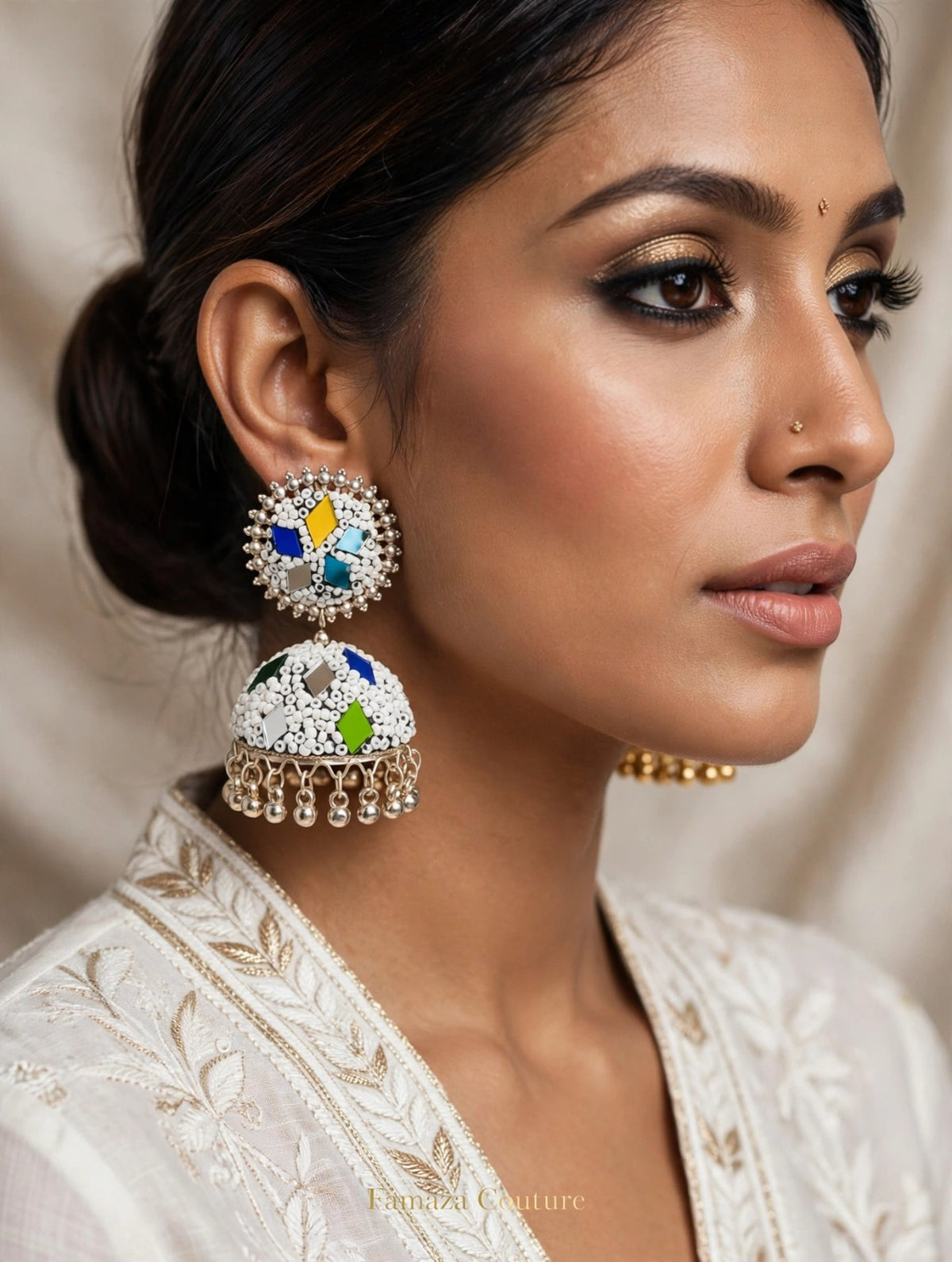 White multi-color meenakari mirror jhumka — cobalt blue, yellow, turquoise, green accents, silver bead border, gold-tone ghungroo drops, worn with white gold-embroidered outfit — Famaza Couture.
