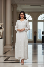 A woman modeling a long white embroidered kurta in a grand, elegant hall with columns and arched windows.